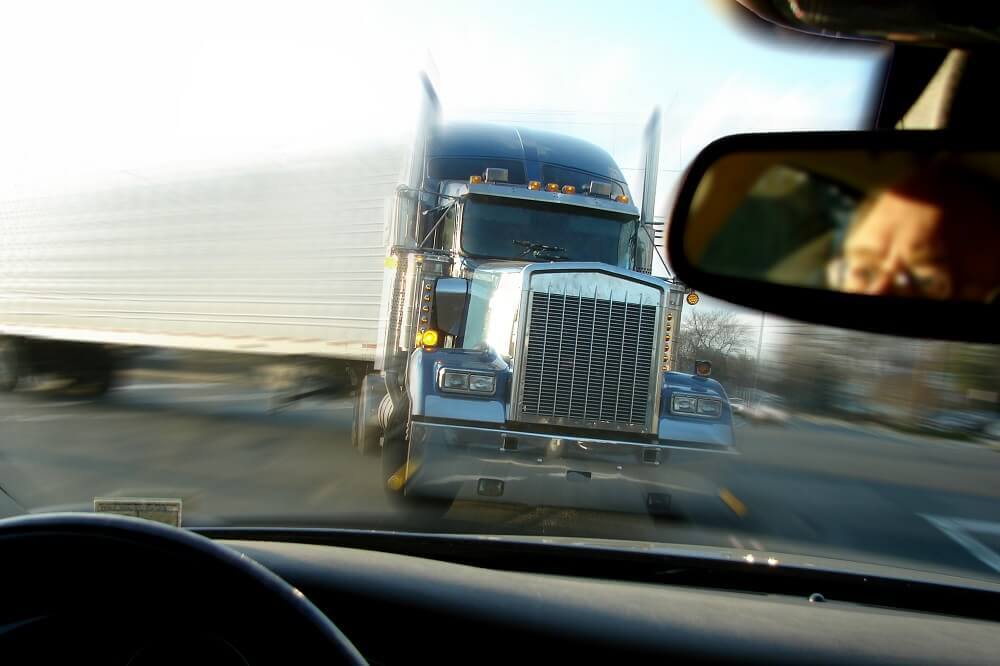 Truck seen in rearview mirror of car making turn in highway.