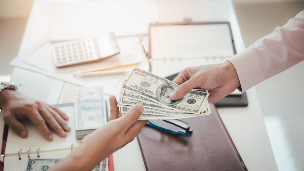 A shot of someone handling another person cash to represent how much a personal injury case might be worth